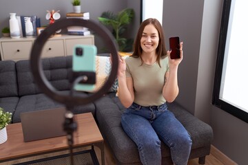 Beautiful brunette woman recording vlog tutorial with smartphone at home looking positive and happy...