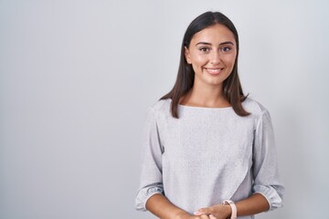 Young hispanic woman standing over white background with hands together and crossed fingers smiling...