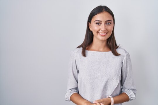 Young hispanic woman standing over white background with hands together and crossed fingers smiling relaxed and cheerful. success and optimistic