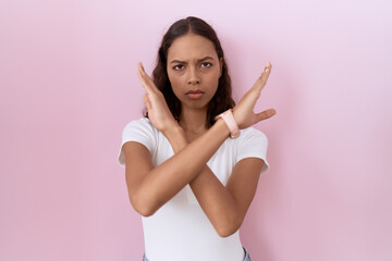 Young hispanic woman wearing casual white t shirt rejection expression crossing arms doing negative...