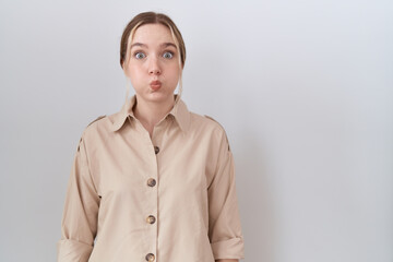 Young caucasian woman wearing casual shirt puffing cheeks with funny face. mouth inflated with air,...