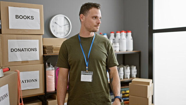 Handsome hispanic man with beard wearing lanyard in warehouse with donations boxes
