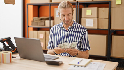 A mature businessman counts money at his warehouse workstation, looking focused and professional.