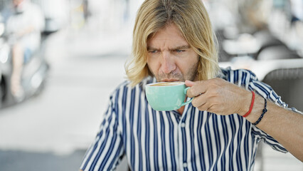 A man with long blond hair sipping coffee at an outdoor urban cafe captures a relaxed lifestyle...