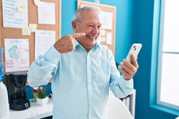 Naklejka na ściany i meble Senior man with grey hair working at the office doing video call with smartphone smiling happy pointing with hand and finger