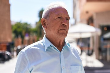 Middle age grey-haired man looking to the side with serious expression at coffee shop terrace