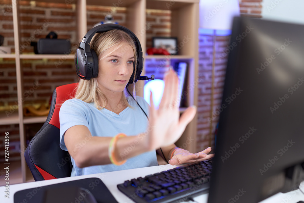 Poster young caucasian woman playing video games wearing headphones doing stop sing with palm of the hand. 