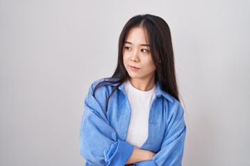 Fototapeta premium Young chinese woman standing over white background looking to the side with arms crossed convinced and confident