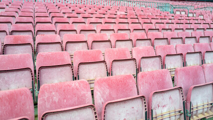 Empty and weathered worn down stadium seating in lightened red and pink tones after year of exposure to weather outdoors in daylight. background graphic design resource