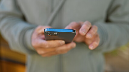Close-up of a mature man's hands using a smartphone on a blurred urban street background.