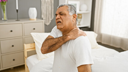 Obraz premium A middle-aged man in pain holding his neck in a well-lit modern bedroom