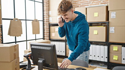 Young hispanic man ecommerce business worker using computer talking on smartphone at office