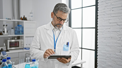 Young hispanic grey-haired man scientist using touchpad at laboratory
