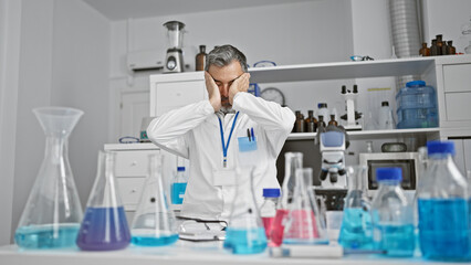 Fototapeta premium Stressed out grey-haired, young hispanic man, a professional scientist, under the microscope's spell, caught in overwork at an indoor laboratory