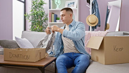 Young man sorting clothes into donation box in a cozy living room.