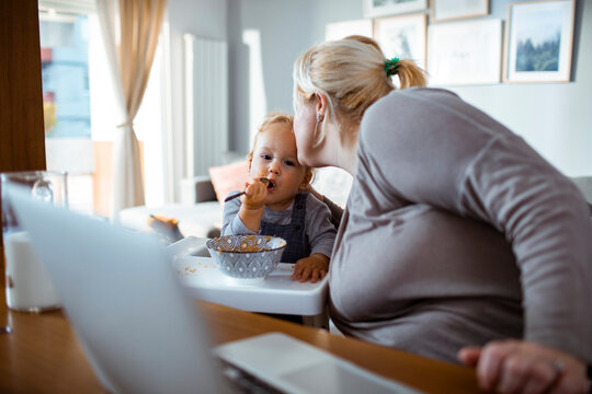 Young single mother using a laptop with her toddler son baby next to her