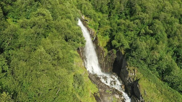 A large beautiful waterfall in the middle of the forest on a sunny evening. Juicy green colors.