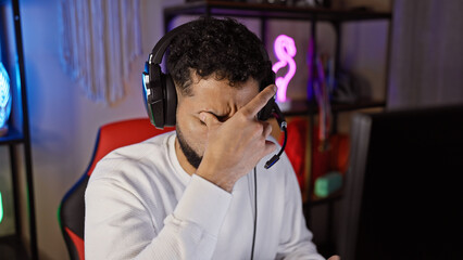 Hispanic man with headphones in gaming room looking stressed during nighttime