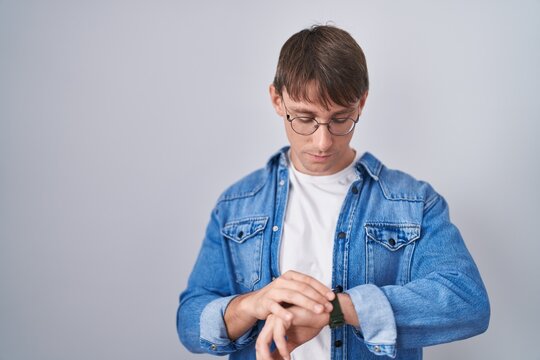 Caucasian blond man standing wearing glasses checking the time on wrist watch, relaxed and confident