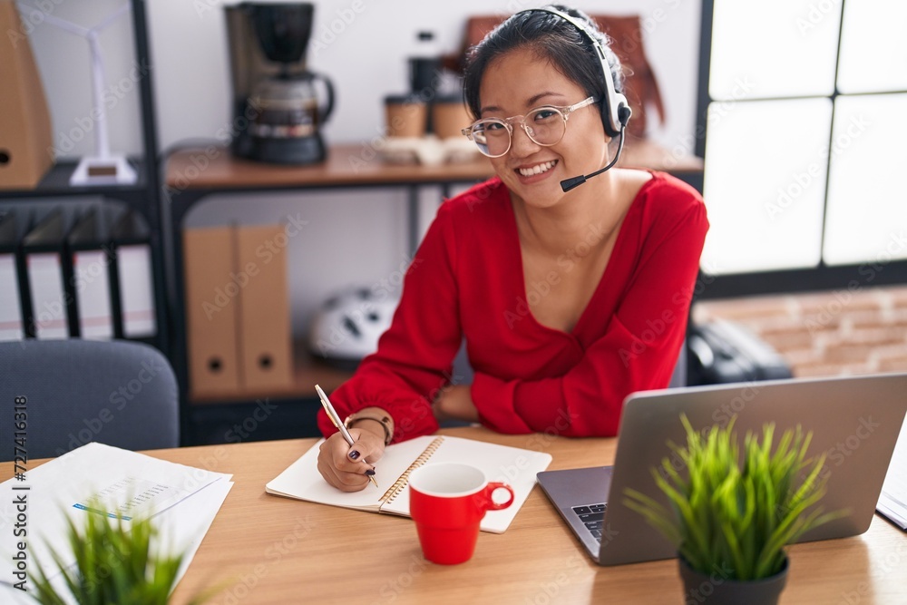 Wall mural young chinese woman call center agent writing on notebook working at office