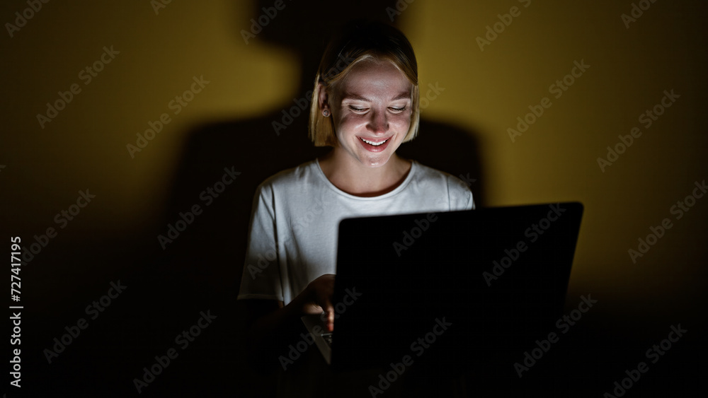 Wall mural young blonde woman using laptop smiling over isolated yellow background