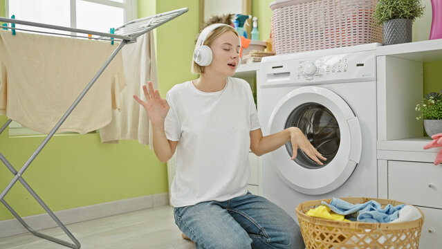 Young blonde woman listening to music and dancing at laundry room