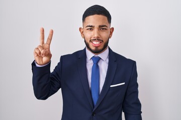 Young hispanic man wearing business suit and tie showing and pointing up with fingers number two while smiling confident and happy.