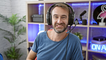 Smiling bearded man with headphones in a modern gaming room home office at night.
