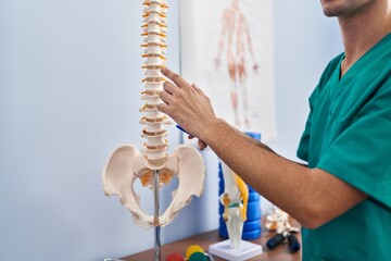 Young caucasian man physiotherapist touching anatomical model of spinal column at rehab clinic