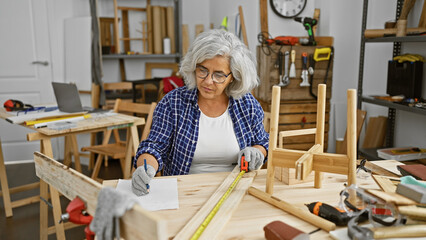 Mature woman measuring wood with tape in a cluttered carpentry workshop