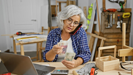 A grey-haired woman examines zloty banknotes in a carpentry workshop.