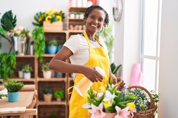 Middle age african american woman florist using diffuser watering plant at flower shop