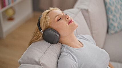 Young blonde woman listening to music relaxed on sofa at home