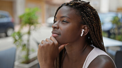 African american woman listening to music sitting on table thinking at coffee shop terrace