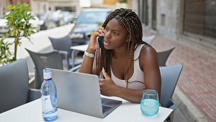 African american woman talking on smartphone sitting on table at coffee shop terrace