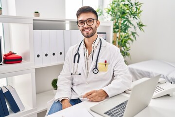 Young hispanic man doctor smiling confident using laptop at clinic