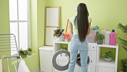 Young latin woman listening to music washing clothes at laundry room