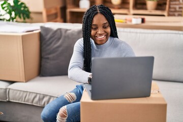 African american woman using laptop sitting on sofa at new home