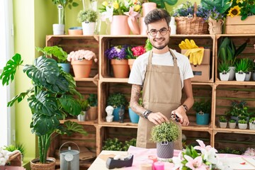 Young hispanic man florist cutting plant at flower shop