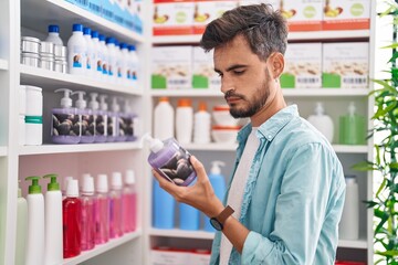 Young hispanic man customer reading label gel hands bottle at pharmacy