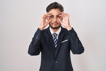 Young hispanic man with tattoos wearing business suit and tie trying to open eyes with fingers, sleepy and tired for morning fatigue