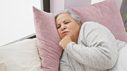 A grey-haired woman appears uncomfortable while lying in a bedroom, suggesting insomnia or sickness.