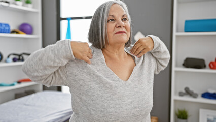 Fototapeta premium A mature woman exercises in a rehab clinic, wearing casual clothing in a well-lit therapy room.
