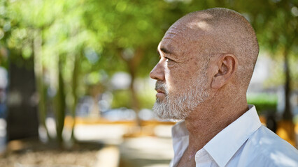 A contemplative middle-aged man with grey beard and bald head in a serene park setting.