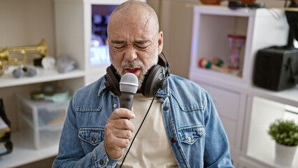 Bald man singing into microphone with headphones in living room, showing passion for music.