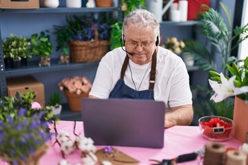 Middle age grey-haired man florist using laptop and headphones at florist