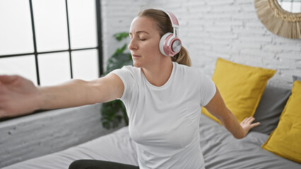 Obraz premium Beautiful, young blonde woman concentrating on her morning yoga exercise, sitting in serene calmness on her bed in cozy bedroom, attuning balance and wellness.