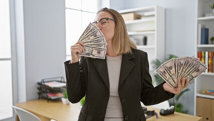 In the office, a beautiful blonde woman kissing dollars, young, confident business executive...