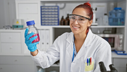 Inside the bustling lab, a confident young redhead scientist, beaming with a smile, expertly...