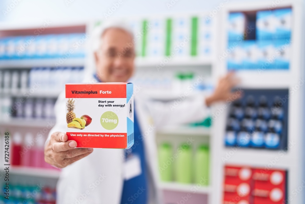 Sticker middle age grey-haired man pharmacist smiling confident holding vitamin package at pharmacy